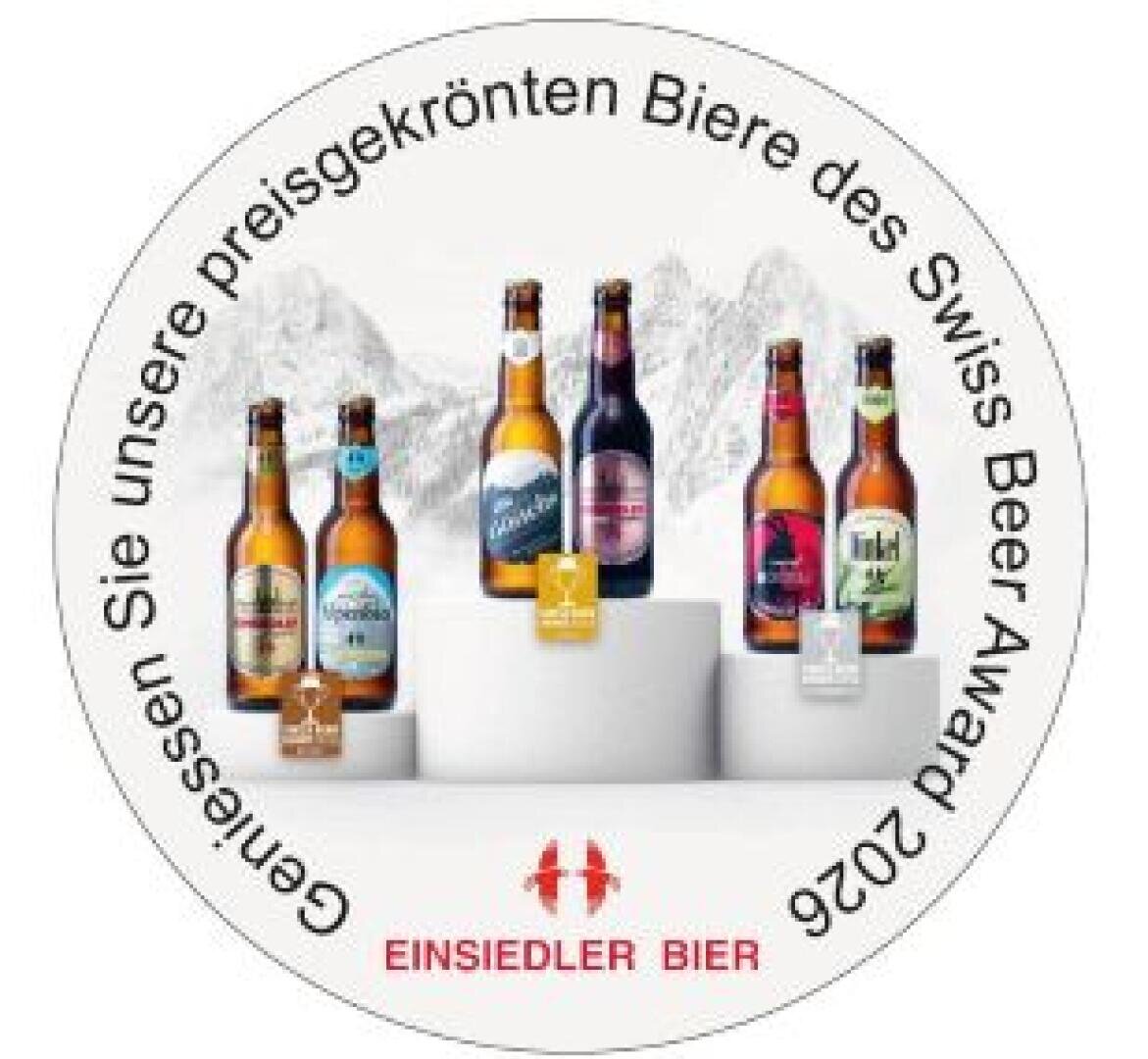 Sechs Flaschen Einsiedler Bier und drei Dosen sind auf Podesten ausgestellt, im Hintergrund sind schneebedeckte Berge zu sehen. Ein deutscher Text am Rand wirbt für den Schweizer Bierpreis 2026.