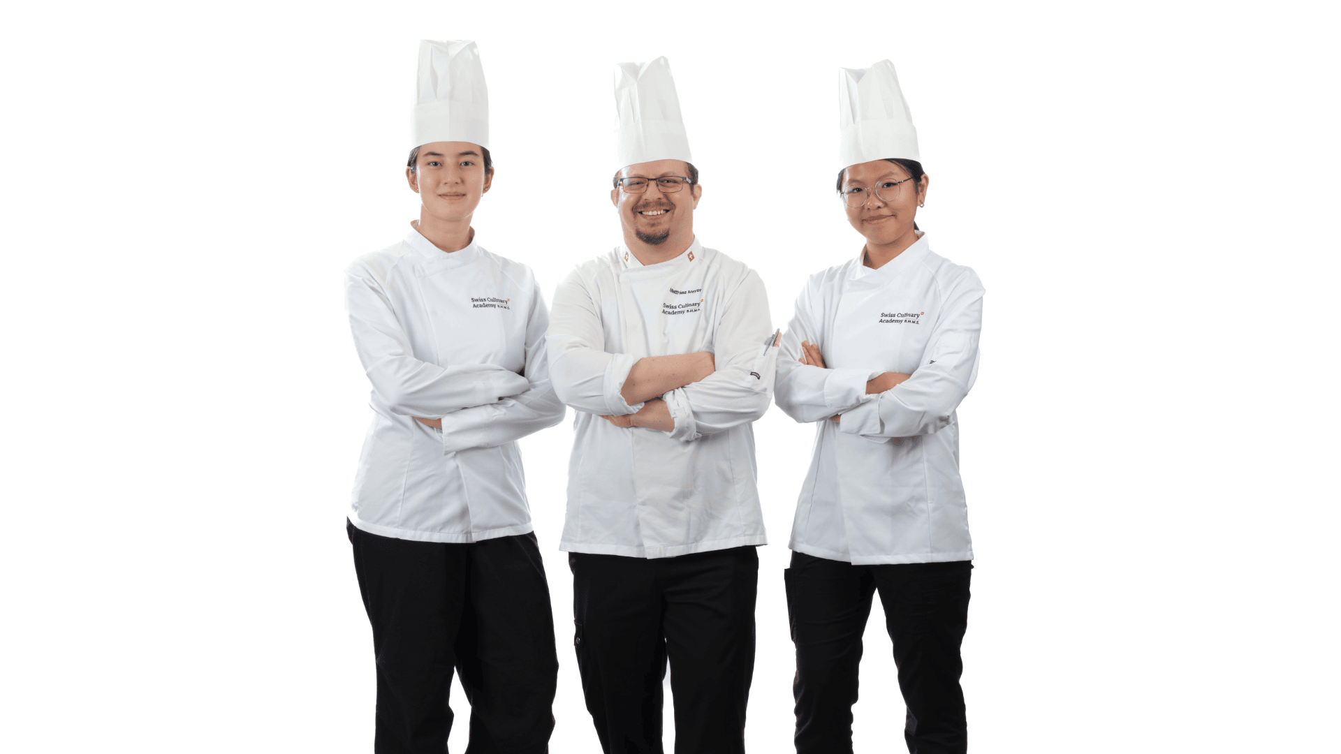 Drei Köche in weißen Uniformen und hohen Kochmützen stehen mit verschränkten Armen da.