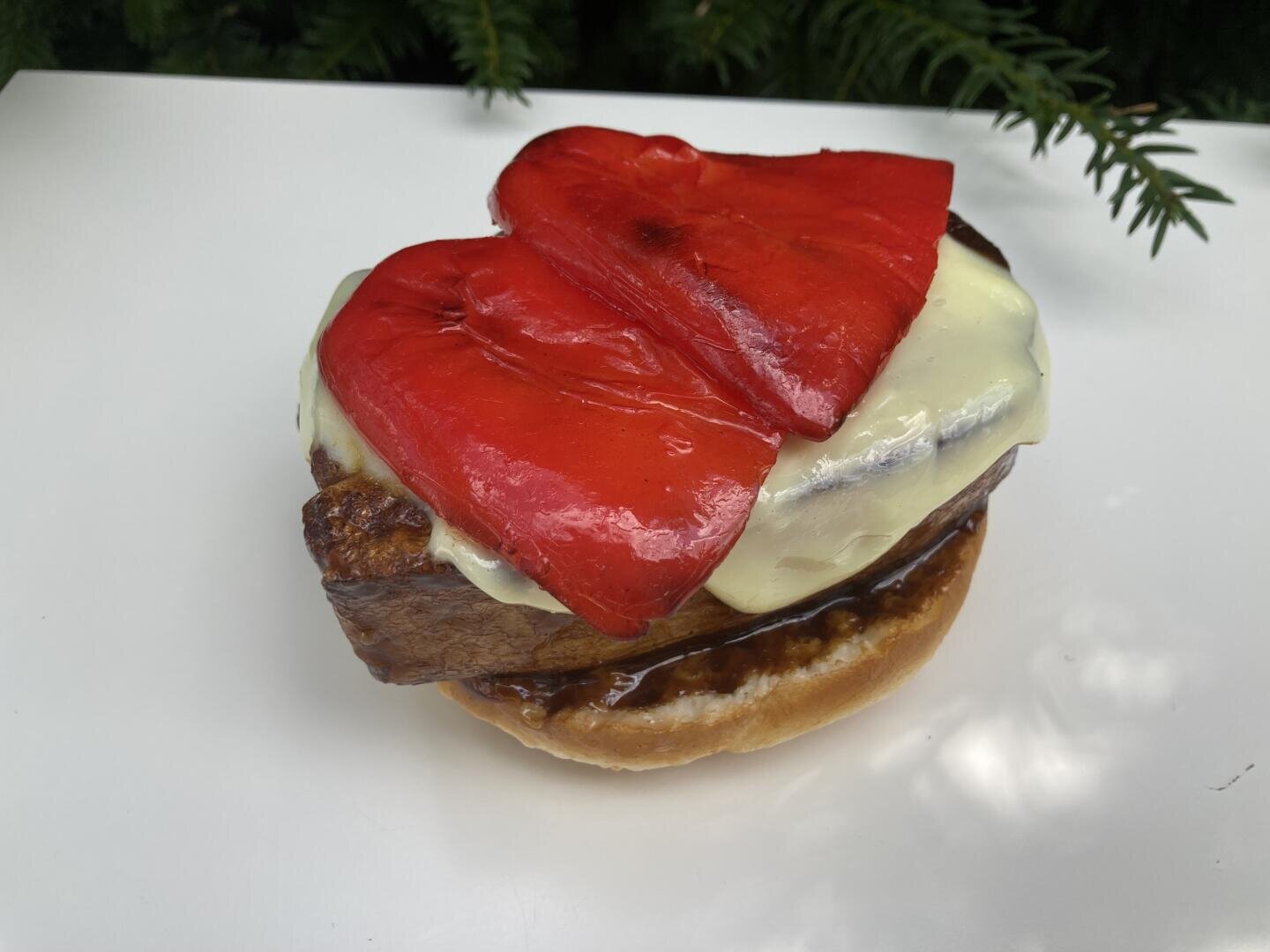 Ein Burger-Patty mit geschmolzenem Käse und gerösteten roten Paprikaschoten auf einem Brötchen.