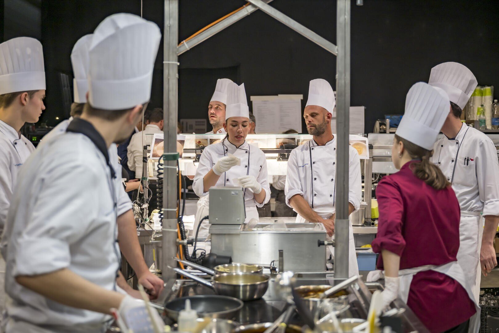 Ein Team von Köchen in weißen Uniformen und hohen Kochmützen bei der Arbeit in einer professionellen Küche.