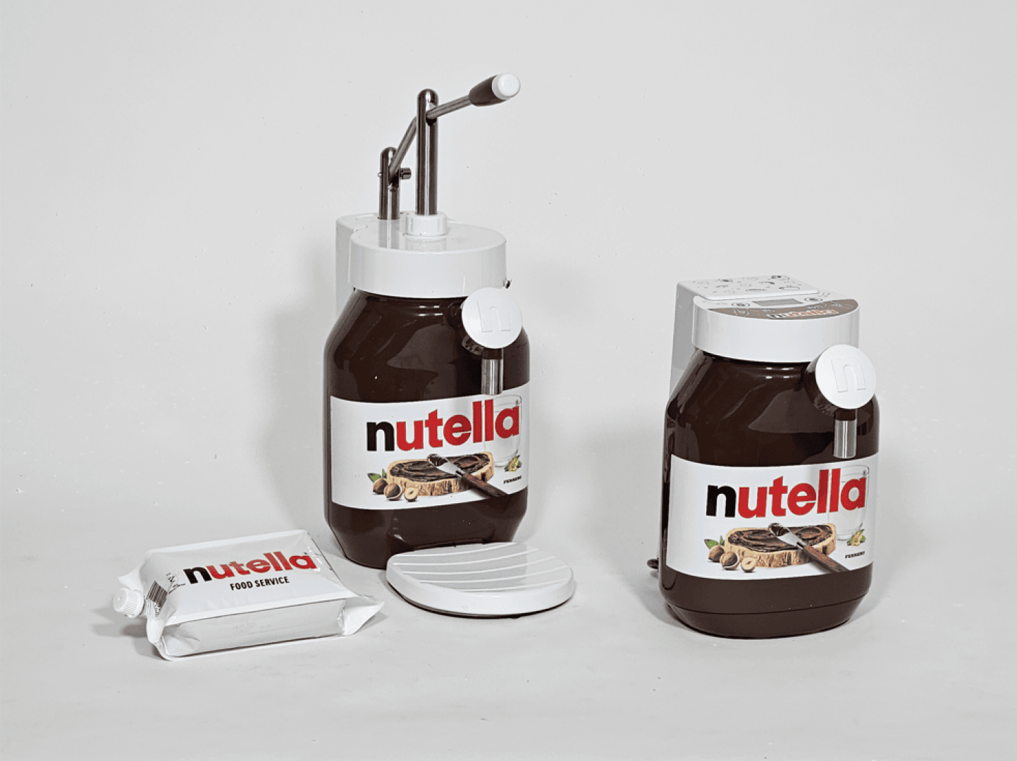Auf einer weißen Fläche stehen zwei große Nutella-Behälter, einer mit einer Pumpvorrichtung und einer mit einem Ausgießer. Außerdem sind eine Verpackung mit der Aufschrift „Nutella Food Service“ und ein runder weißer Deckel zu sehen.