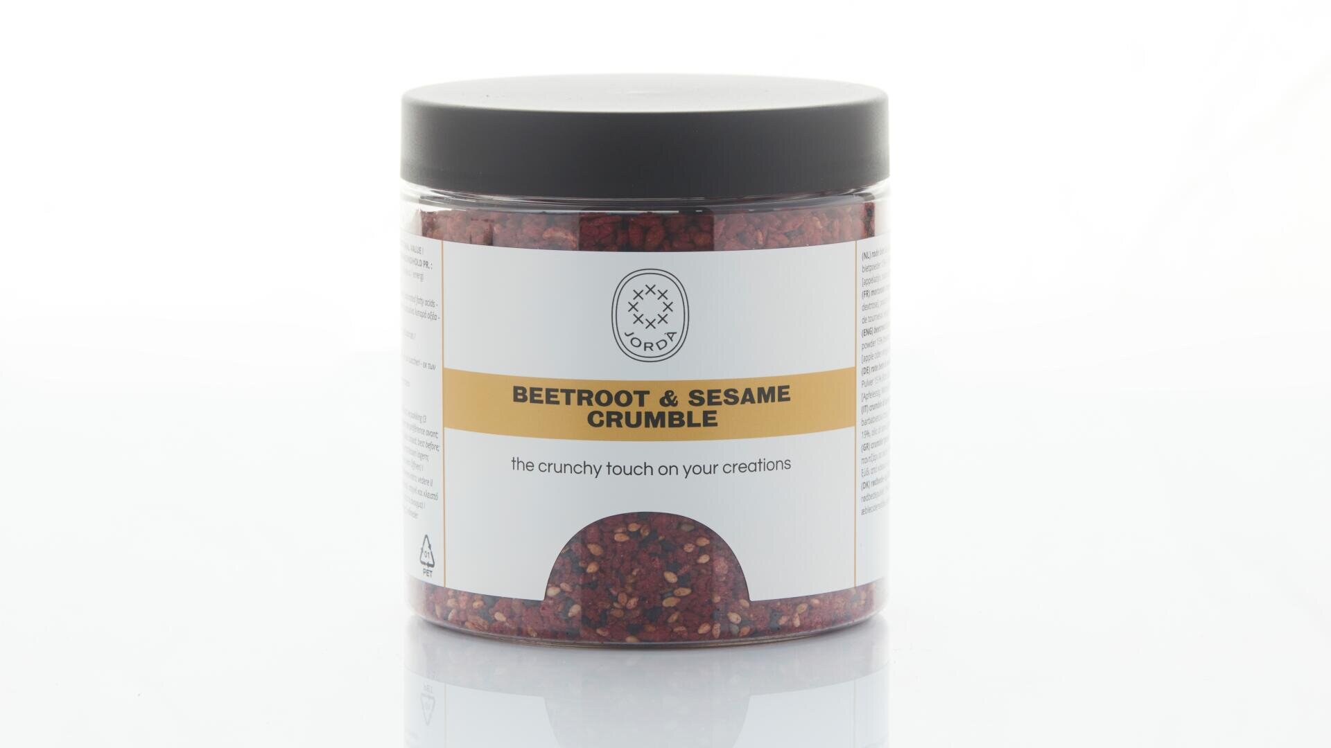 Ein durchsichtiges Plastikglas mit schwarzem Deckel, beschriftet mit „Rote Bete & Sesam-Streusel“. Das Etikett ist größtenteils weiß mit gelben Akzenten und enthält Informationen zum Produkt. Das Glas enthält rötliche Streuselstücke.