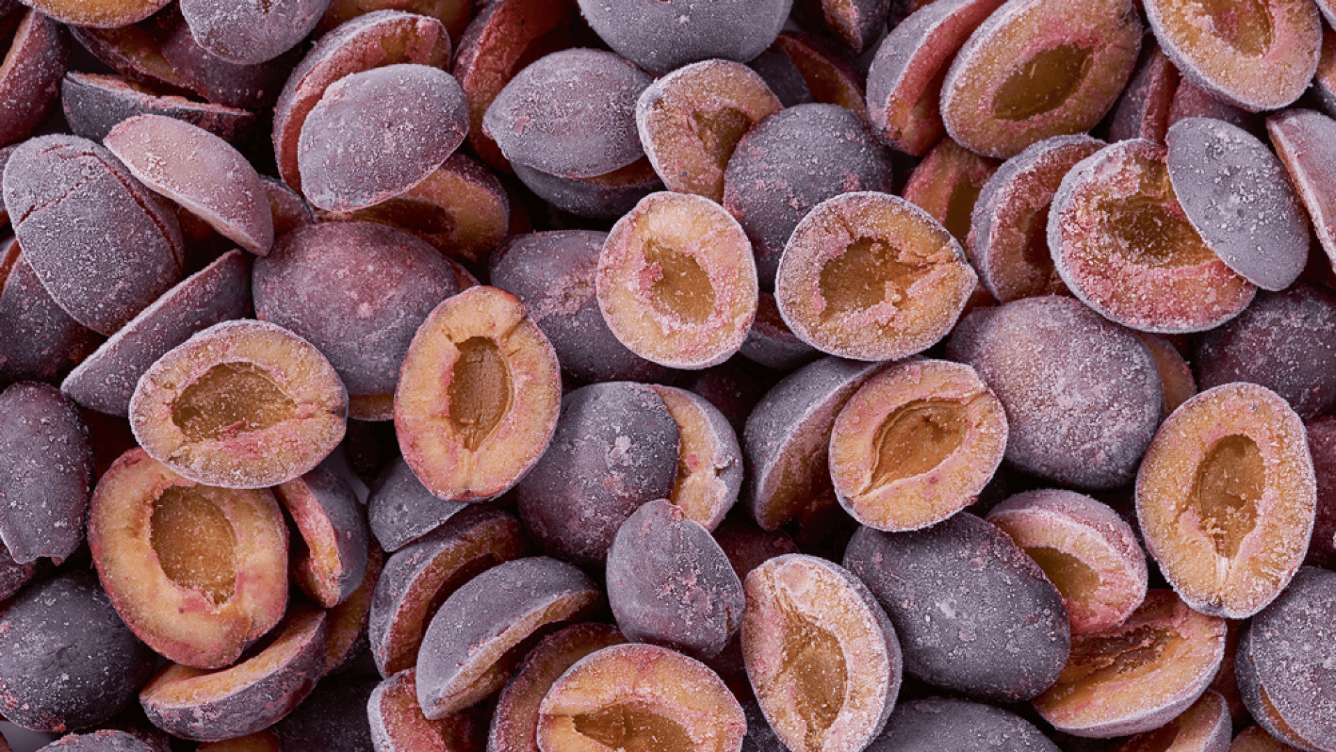 Eine Nahaufnahme von vielen halbierten violetten Pflaumen, bei denen die Kerne entfernt wurden. Die Pflaumen scheinen gefroren zu sein, denn auf ihrer Schale und ihrem Fruchtfleisch befindet sich eine Frostschicht.