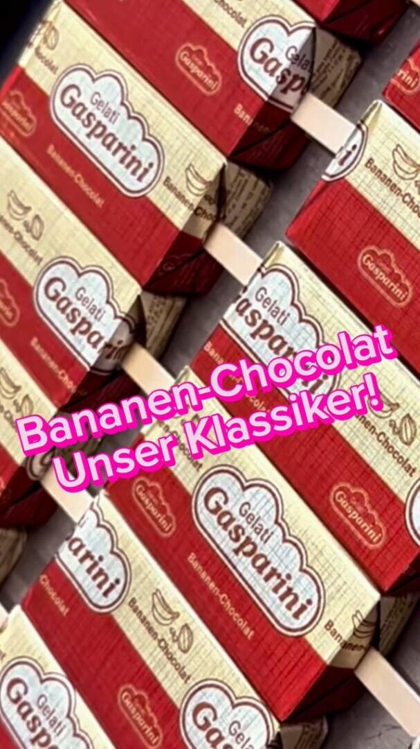 Die Kartons mit „Gaspardi Bananen-Chocolat“ sind schräg gestapelt. In rosa Schrift steht auf Deutsch: „Bananen-Chocolat – Unser Klassiker!“.