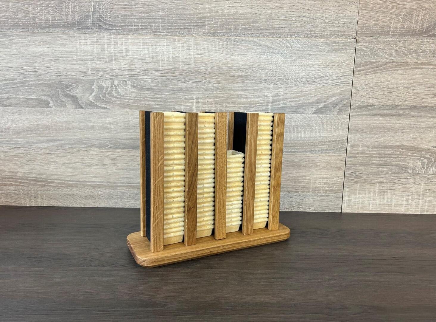 In einem Organizer aus Holz stehen sechs hellbraune, gerippte, rechteckige Gegenstände senkrecht, die an Bücher oder Aktenordner erinnern. Im Hintergrund sind helle Holzvertäfelungen und eine dunkelbraune Tischplatte zu sehen.