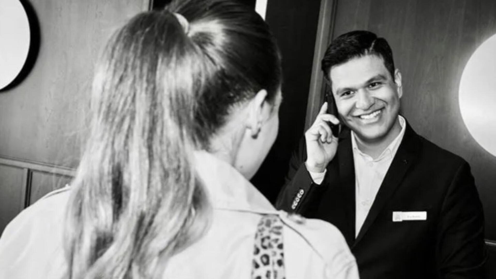 Ein Hotelrezeptionist, der lächelt, während er telefoniert und einem Gast weiterhilft.