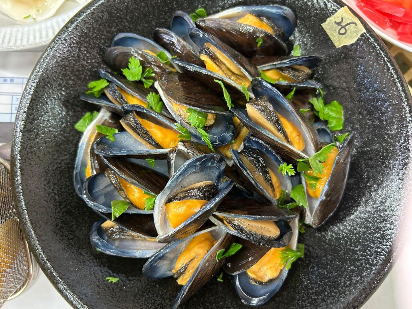 Eine schwarze Schüssel, gefüllt mit gedämpften Muscheln und garniert mit frischer Petersilie.