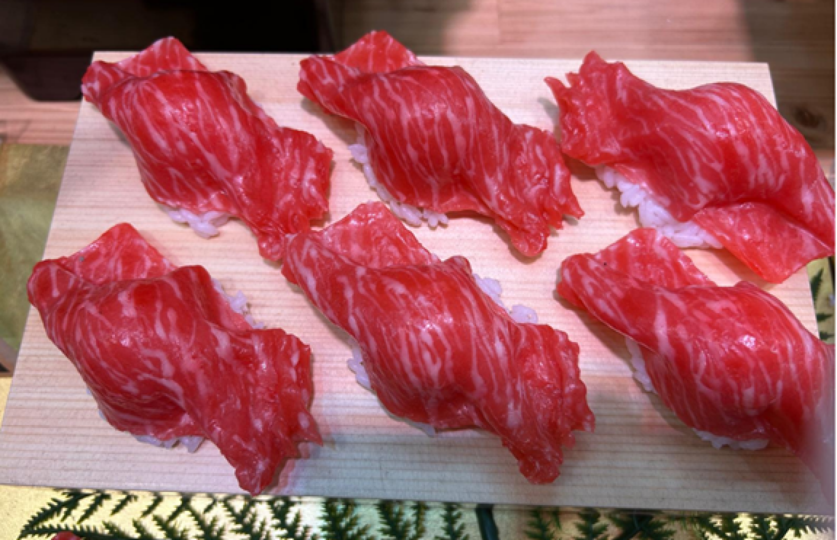Sechs Stück Wagyu-Rindfleisch-Nigiri-Sushi, serviert auf einem Holzbrett.