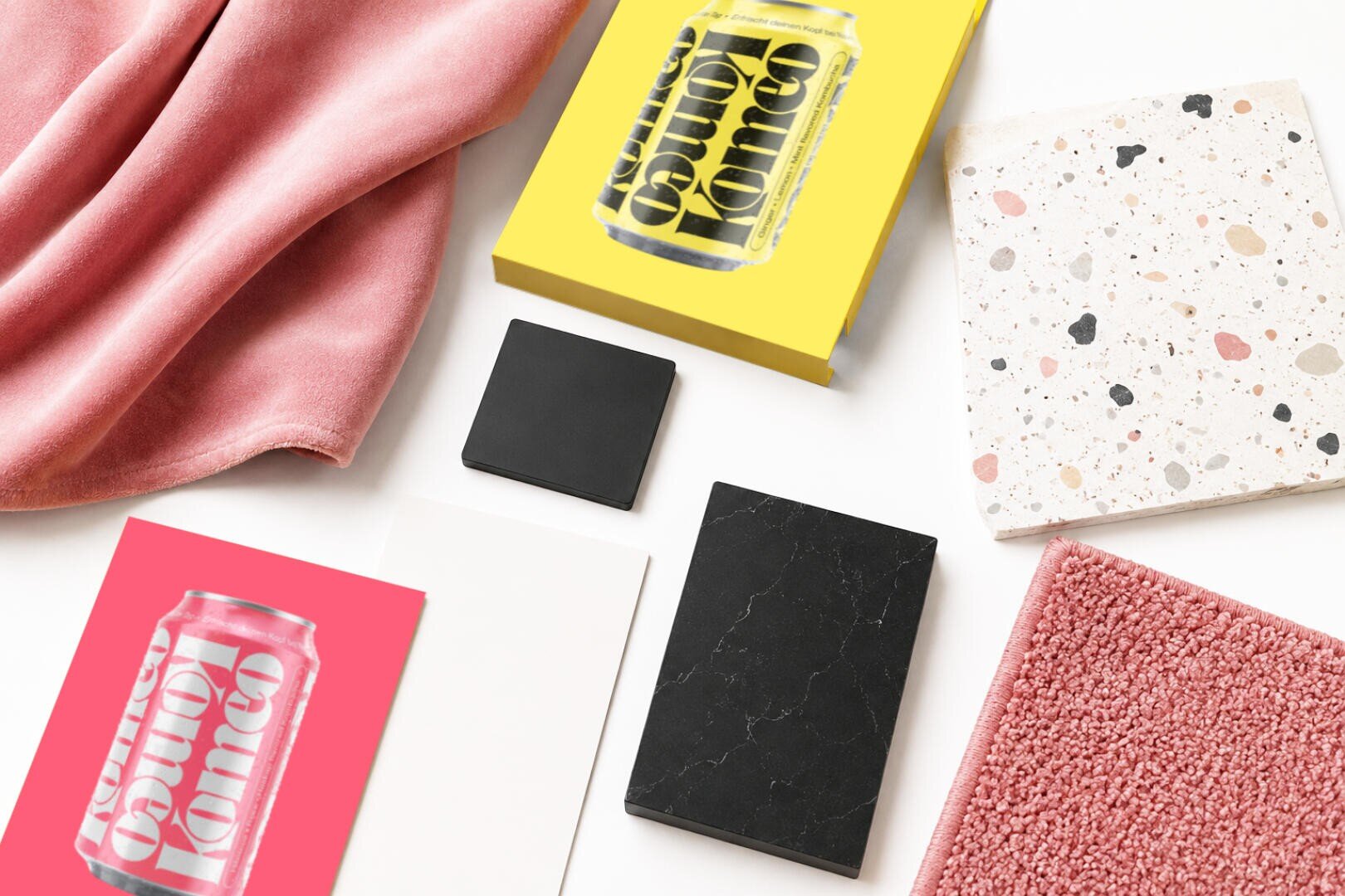 Eine „Flat Lay“-Aufnahme von Designmaterialien: rosa Stoff, rosa Teppich, Terrazzo-Fliesen, schwarz-weiße Fliesen, weißer Karton und zwei Kunstdrucke mit Getränkedosen, eine gelbe und eine rosa.