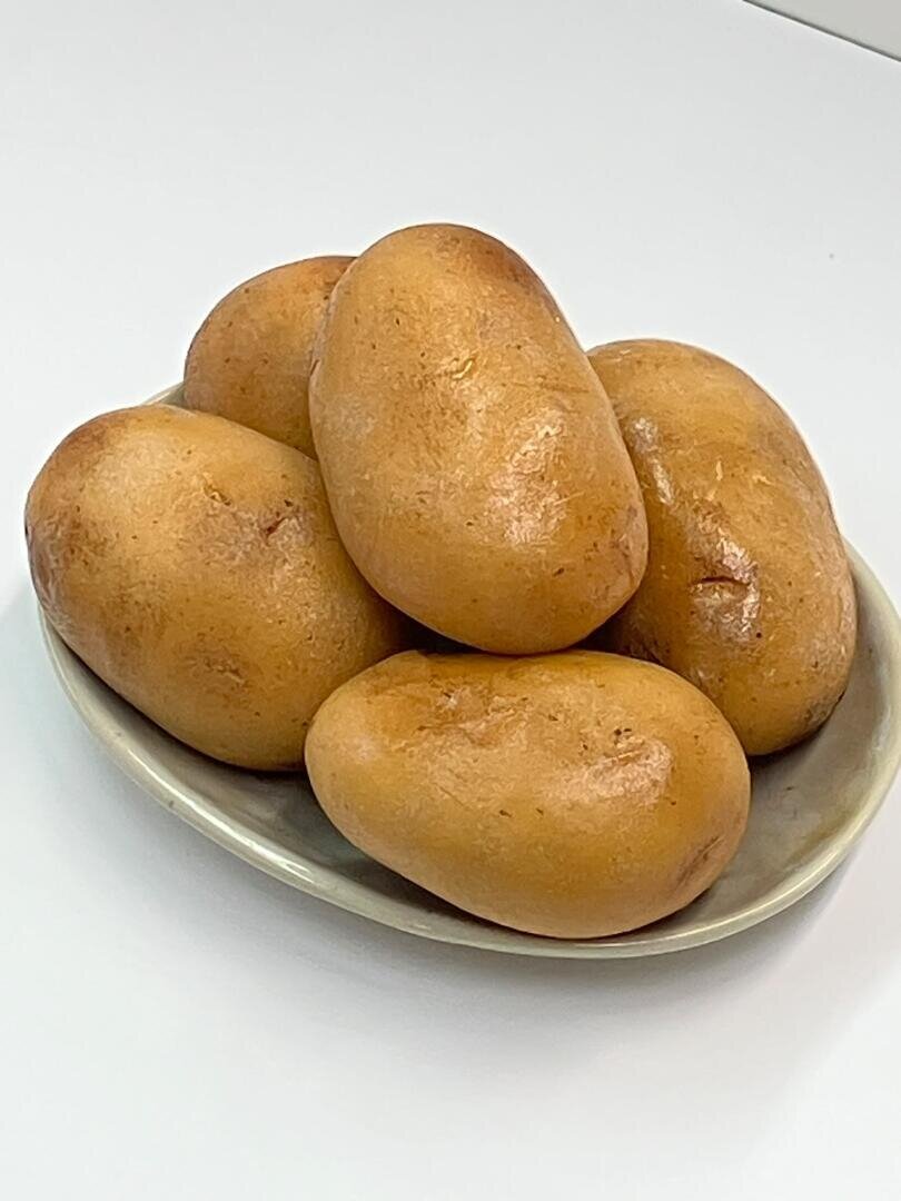 Ein kleiner Teller mit fünf ganzen braunen Kartoffeln.
