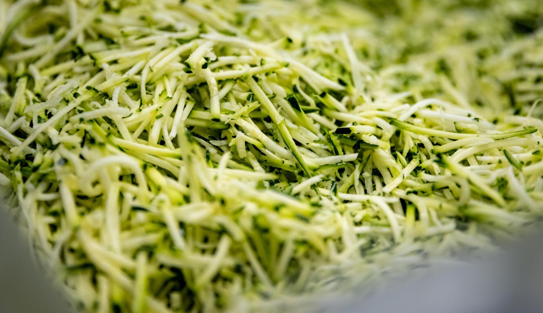 Nahaufnahme eines Haufens geraspelter Zucchini, auf dem dünne, grüne und weiße Streifen zu sehen sind.