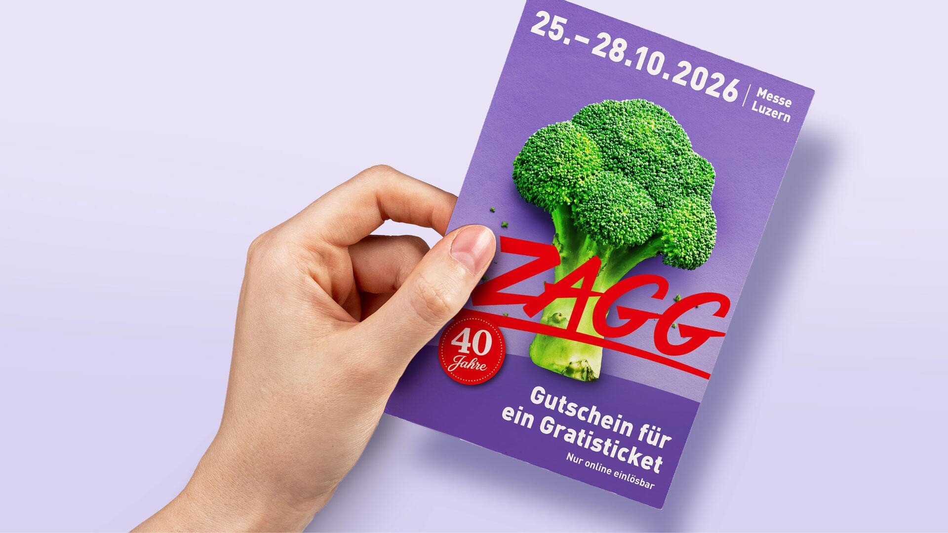 Eine Hand hält einen violetten ZAGG-Veranstaltungsflyer mit einem Brokkoli-Motiv, den Veranstaltungsterminen (25.–28.10.2026), dem Veranstaltungsort (Messe Luzern) und einem Angebot für einen Gutschein für eine Freikarte.