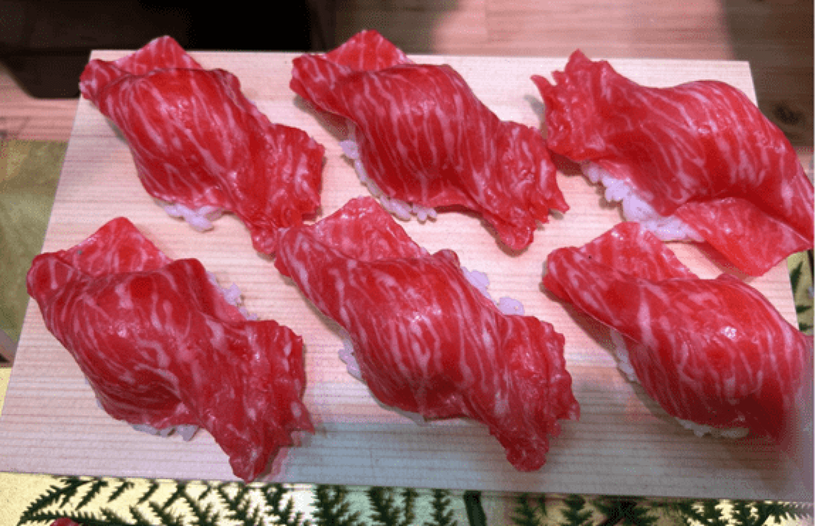 Sechs Stück Wagyu-Rindfleisch-Nigiri-Sushi, serviert auf einem Holzbrett.