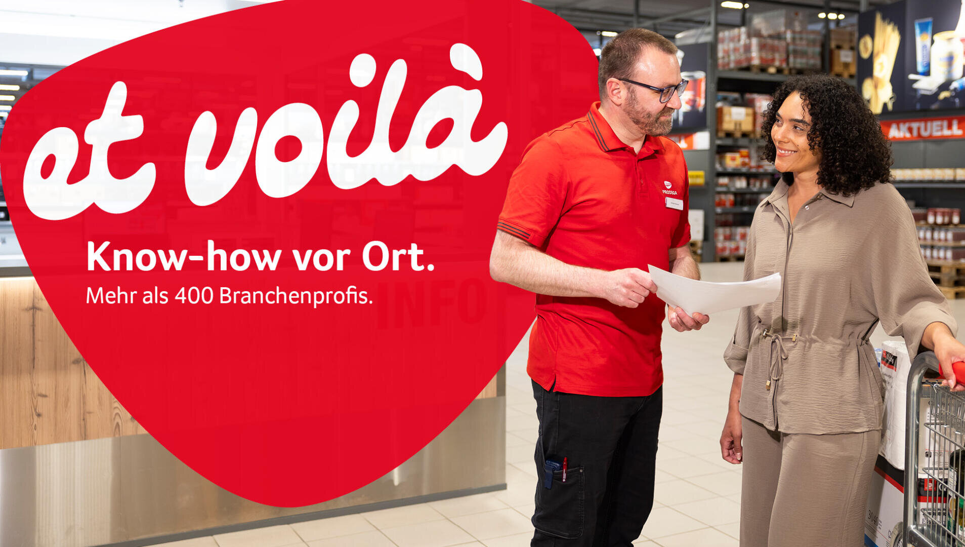 Ein Mann in einem roten Hemd und eine Frau mit lockigem Haar stehen in einem Geschäft, unterhalten sich und lächeln. Der Text lautet: „Et voilà. Know-how vor Ort. Mehr als 400 Branchenprofis…“.