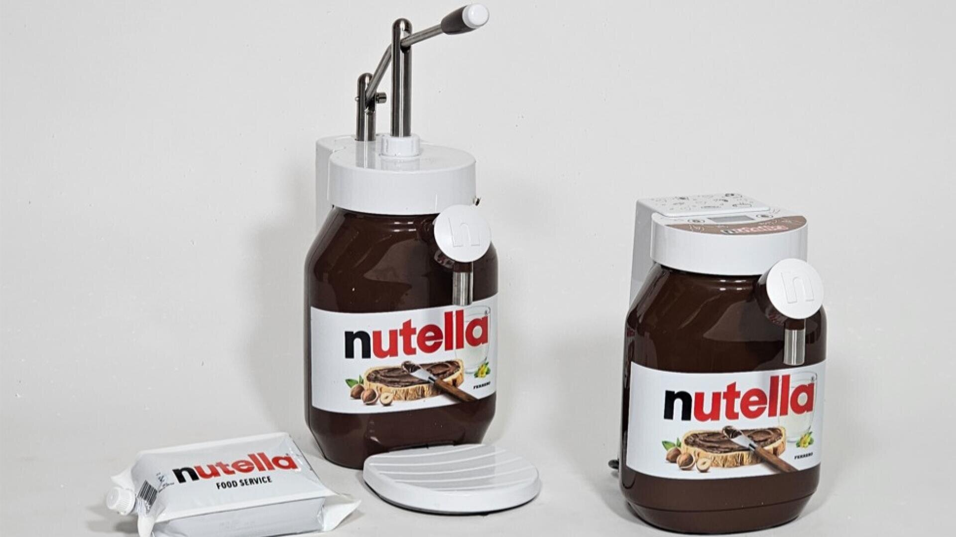 Auf einer weißen Fläche stehen zwei große Nutella-Behälter, einer mit einer Pumpvorrichtung und einer mit einem Ausgießer. Außerdem sind eine Verpackung mit der Aufschrift „Nutella Food Service“ und ein runder weißer Deckel zu sehen.