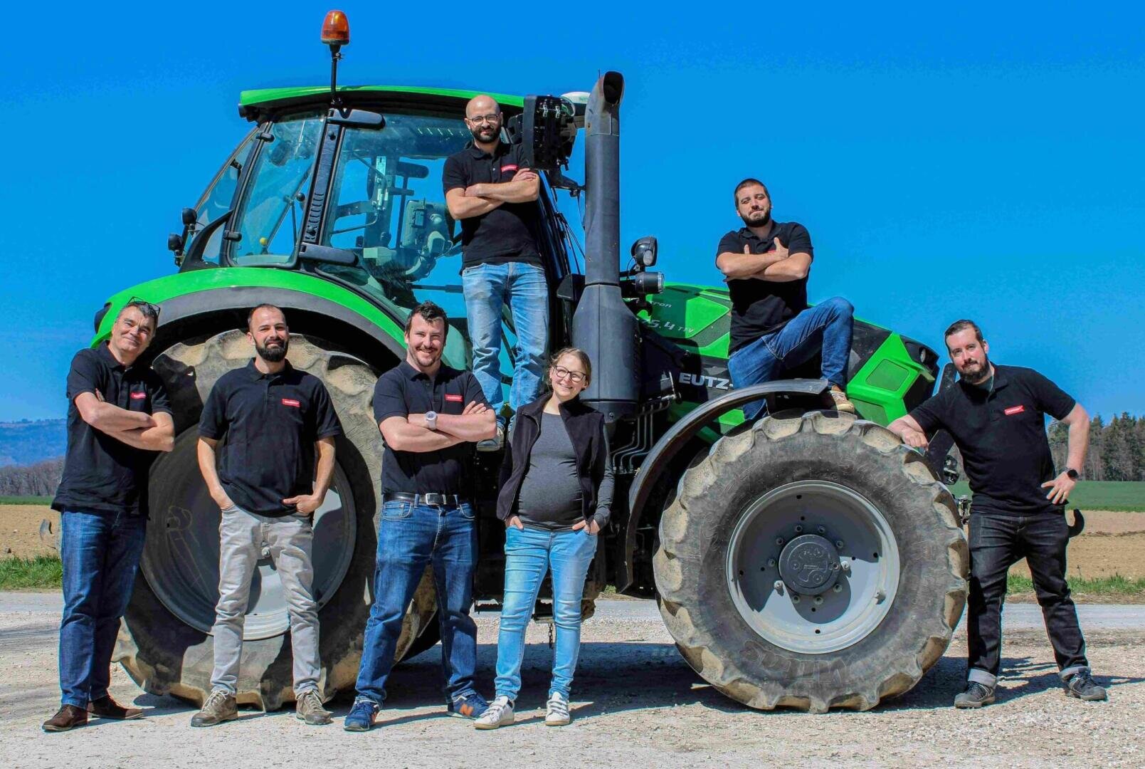 Eine Gruppe von sechs Personen, die vor einem großen grünen Traktor auf einem Feld posieren.