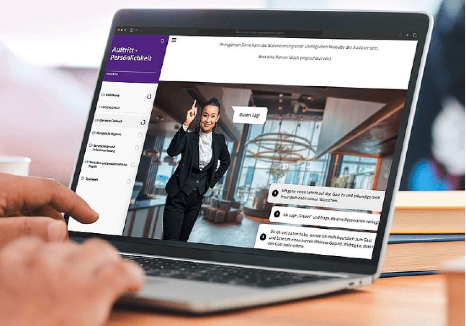 Eine Person benutzt einen Laptop, auf dem ein Online-Schulungskurs in deutscher Sprache angezeigt wird, mit einer winkenden Frau im Anzug, Sprechblasen und einer modernen Bürohalle im Hintergrund.