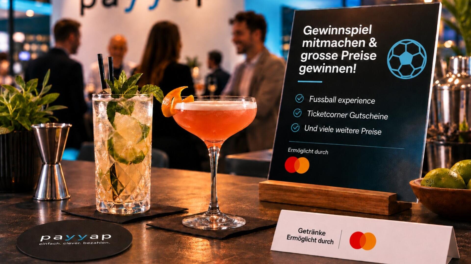 Zwei Cocktails auf einer Bartheke neben einem Schild, das für ein Gewinnspiel zum Thema Fußball mit Mastercard-Logo wirbt.