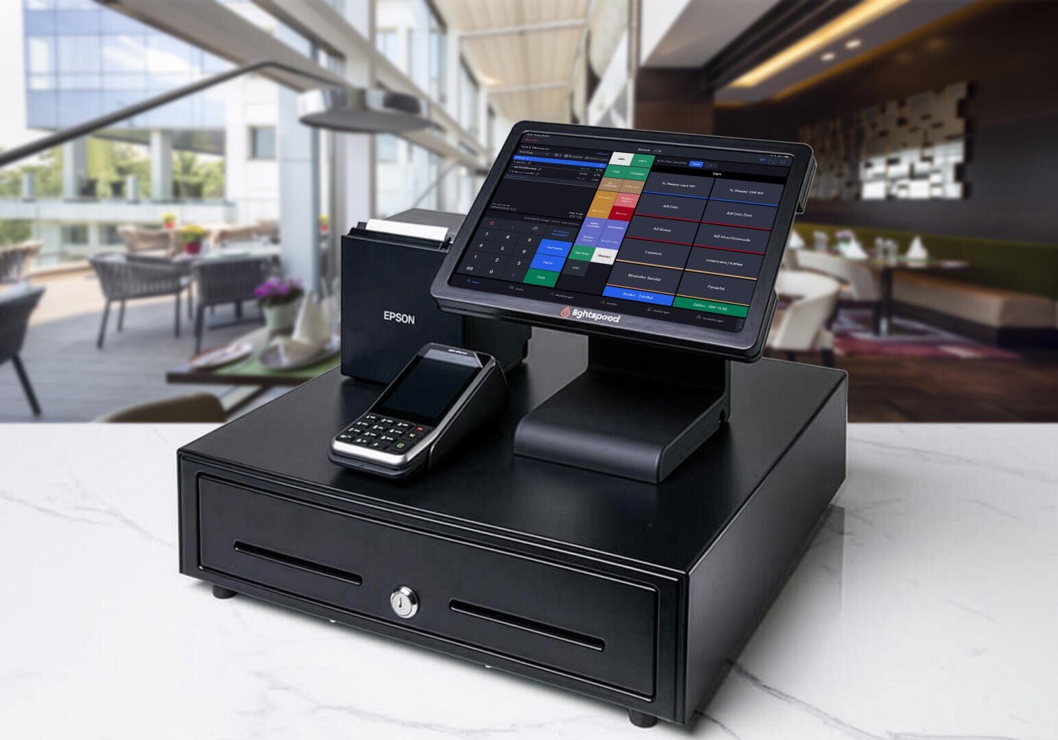 Ein modernes Kassensystem mit Touchscreen, Kartenlesegerät, Drucker und Kassenschublade steht auf einer weißen Theke in einem hellen, stilvollen Restaurant.
