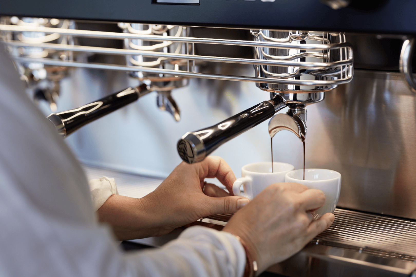 Eine Person hält zwei weiße Espressotassen unter eine Kaffeemaschine, während frischer Espresso in die Tassen gegossen wird.