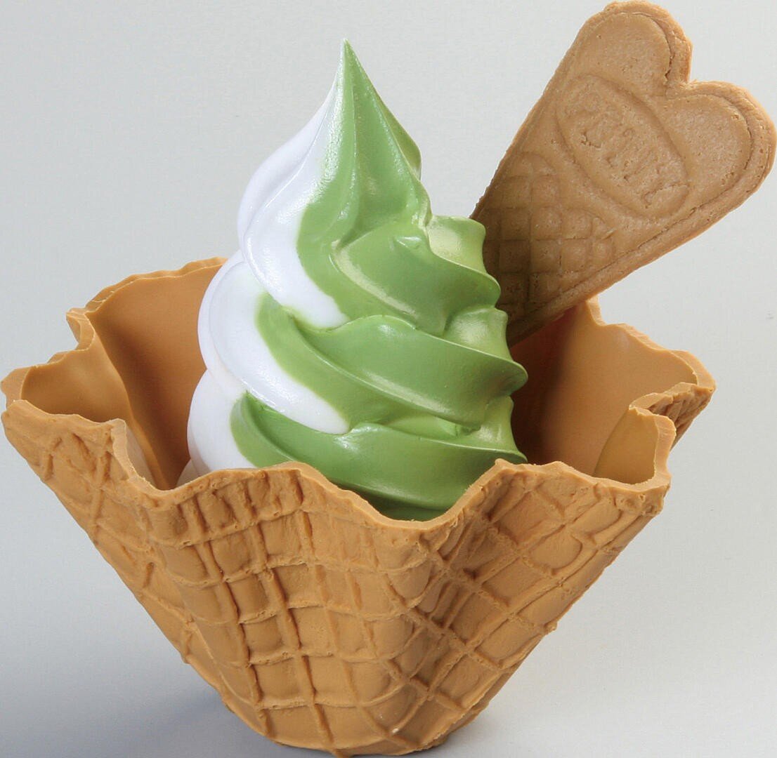 Eine Mischung aus weißem und grünem Matcha-Softeis in einer Waffelschale mit einem herzförmigen Waffelkeks.