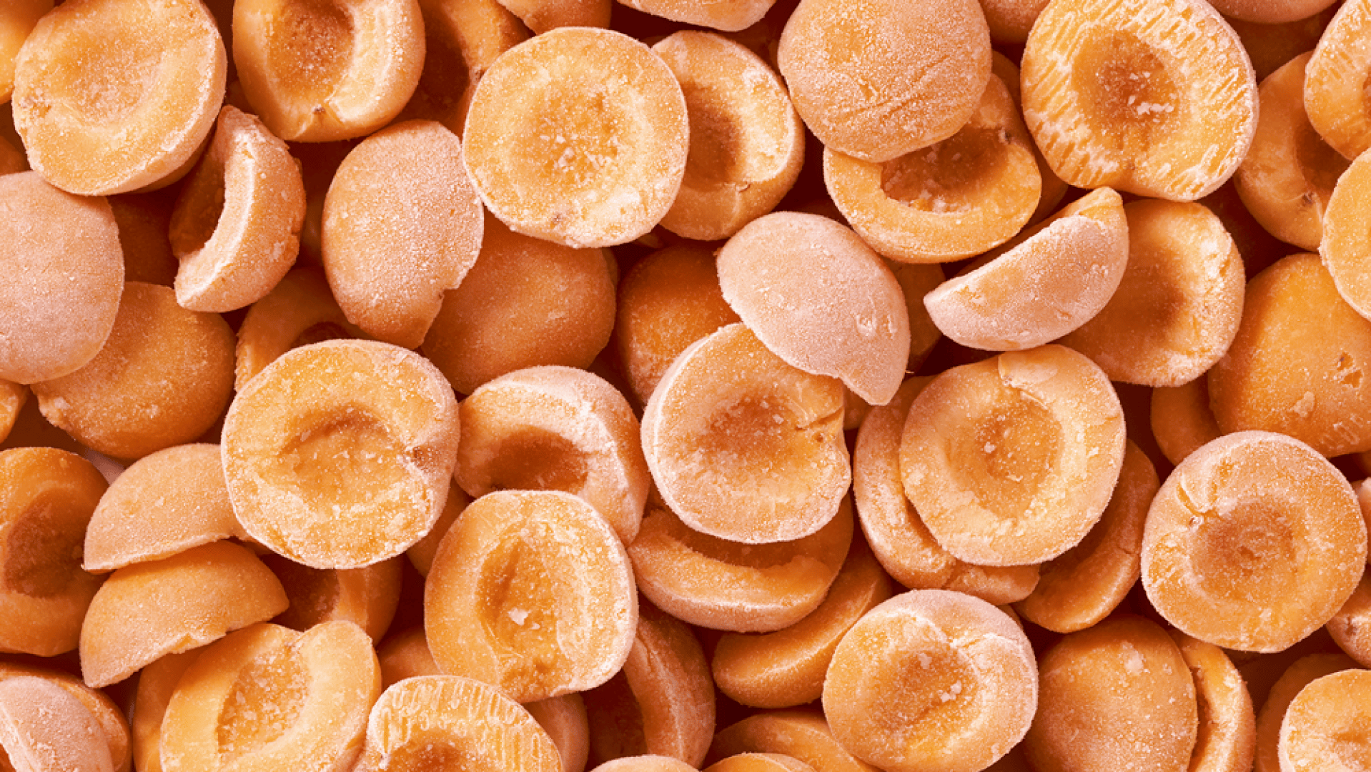 Eine Nahaufnahme vieler halbierter Aprikosen, bei denen die Kerne entfernt wurden, zeigt ihre orange Farbe und ihr frostiges Aussehen, was darauf hindeutet, dass sie gefroren sind.