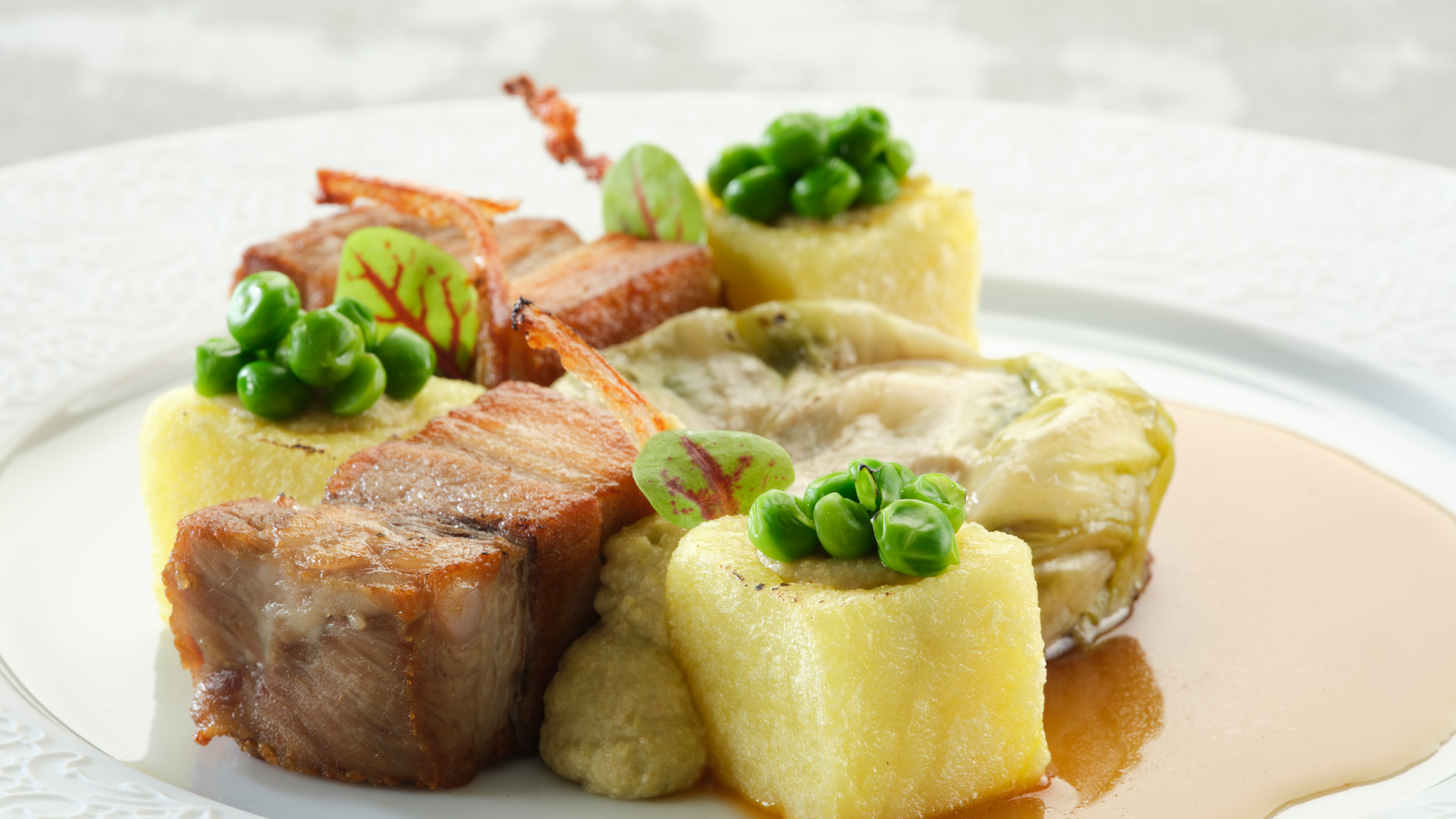 Schweinebauch, serviert mit Polenta-Würfeln, garniert mit grünen Erbsen und dazu geschmorter Kohl in Soße.