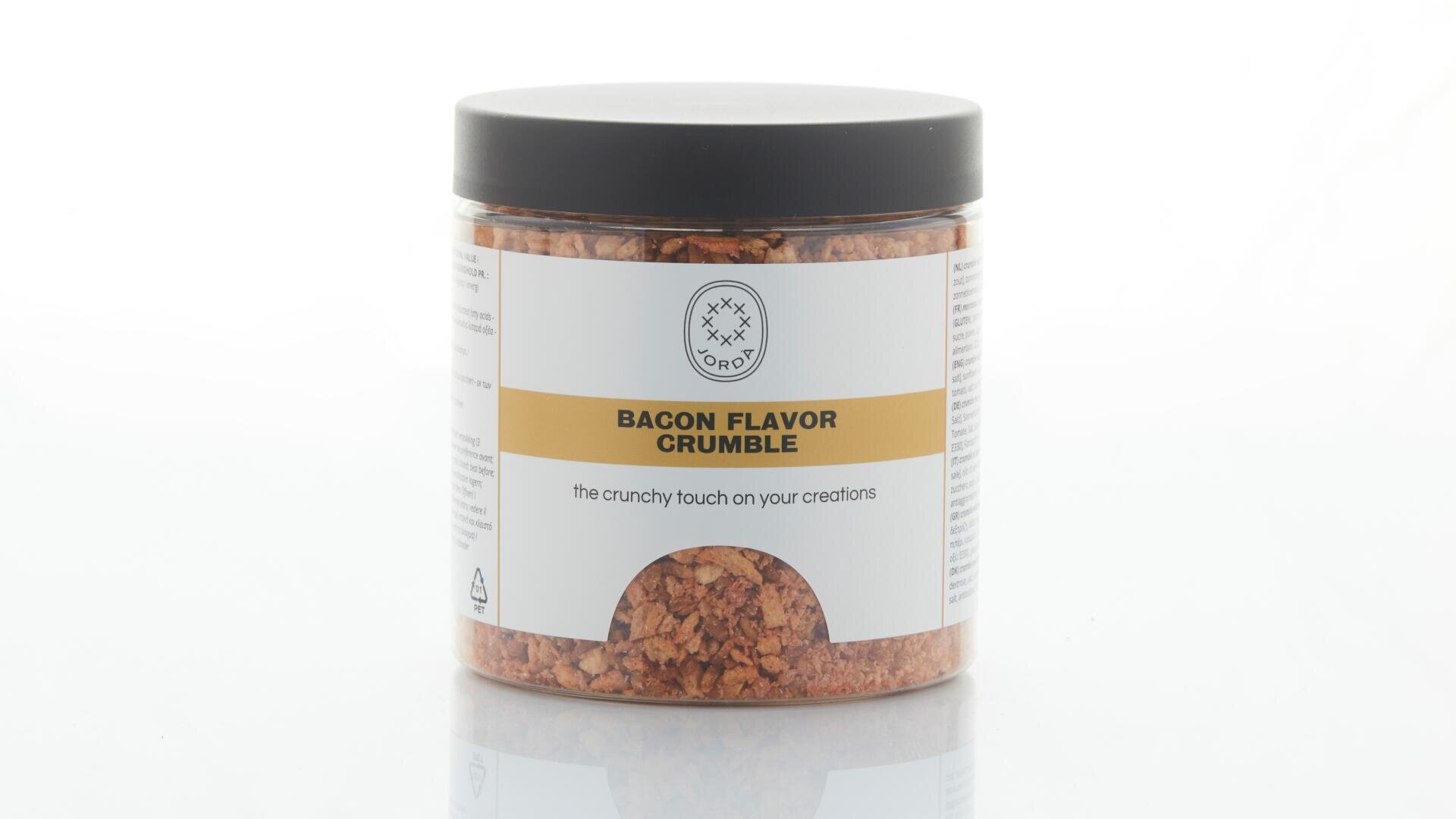 Auf einer weißen Fläche steht ein durchsichtiges Plastikglas mit der Aufschrift „Bacon Flavor Crumble“ und einem schwarzen Deckel. Das Glas enthält kleine, rotbraune Stückchen mit Speckgeschmack.