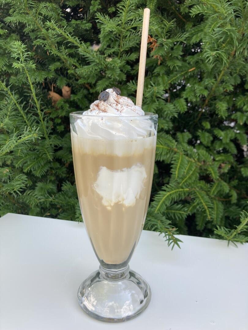 Eiskaffee in einem hohen Glas, garniert mit Schlagsahne, einer Prise Puderzucker und Kaffeebohnen, dazu ein Strohhalm.