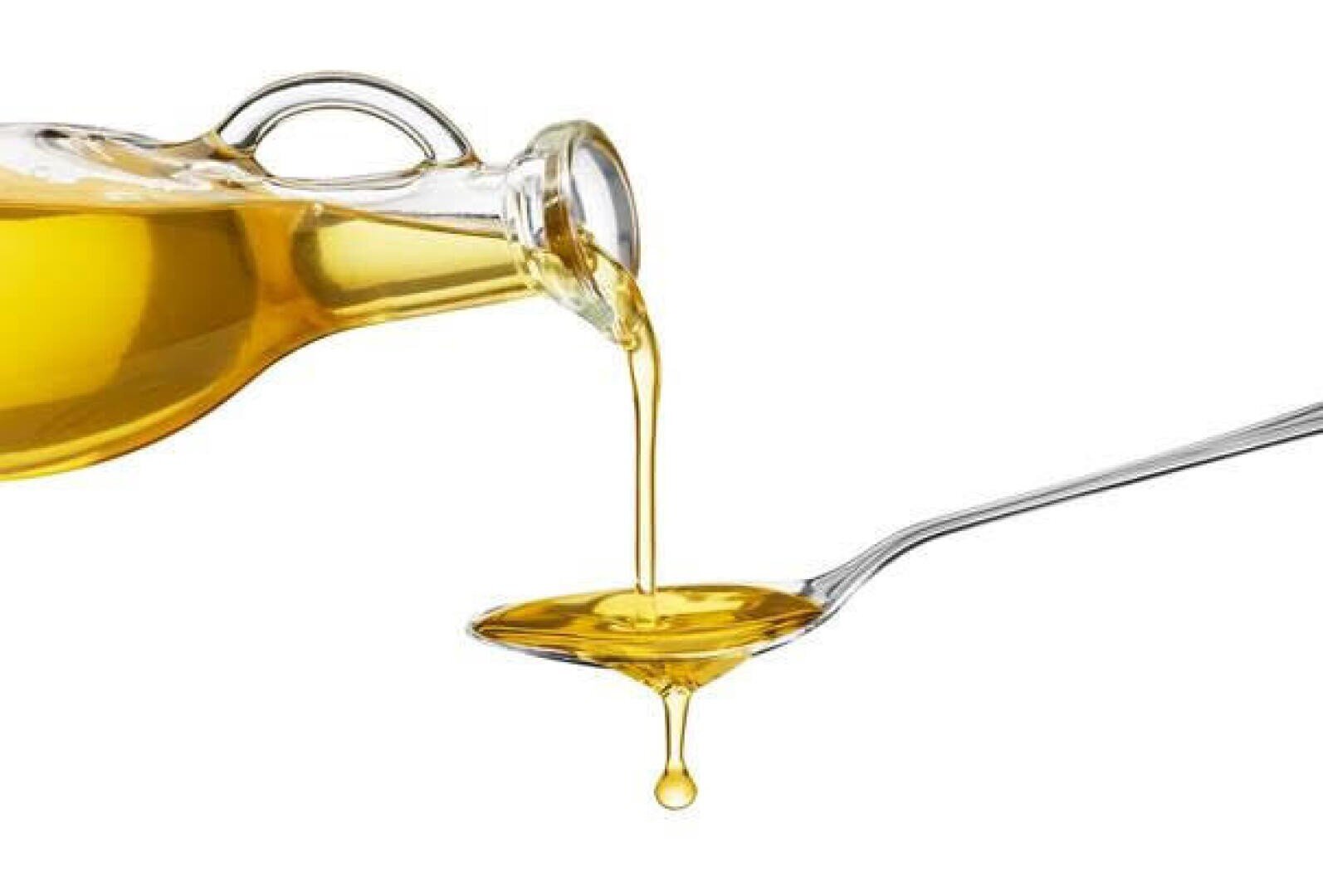 Goldenes Öl wird aus einer Glasflasche in einen silbernen Löffel gegossen, wobei das Öl vom Löffel auf einen weißen Hintergrund tropft.