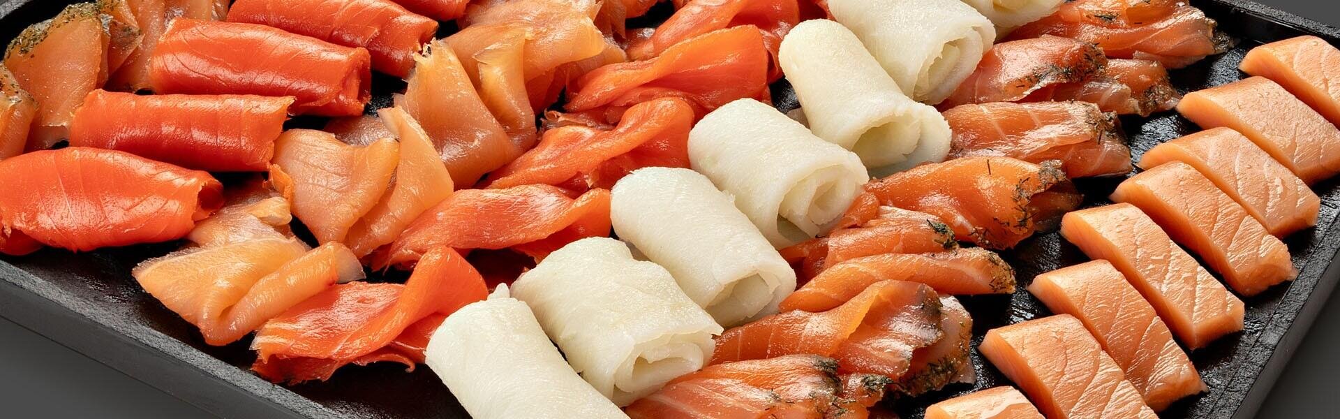 Anrichtung von geräuchertem Lachs in Scheiben und gerolltem Weißfisch auf einer schwarzen Platte.