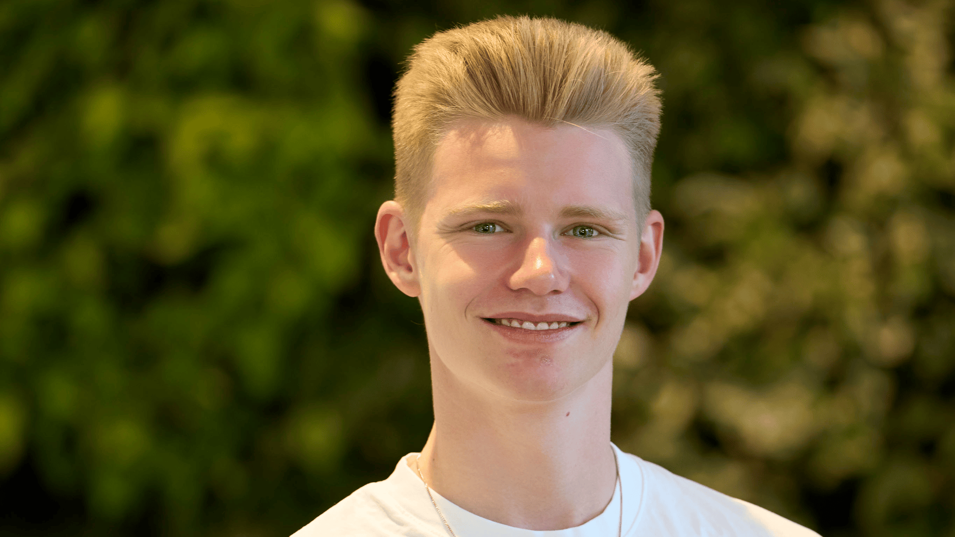Ein Porträtfoto eines jungen Mannes mit kurzen blonden Haaren, der in die Kamera lächelt.