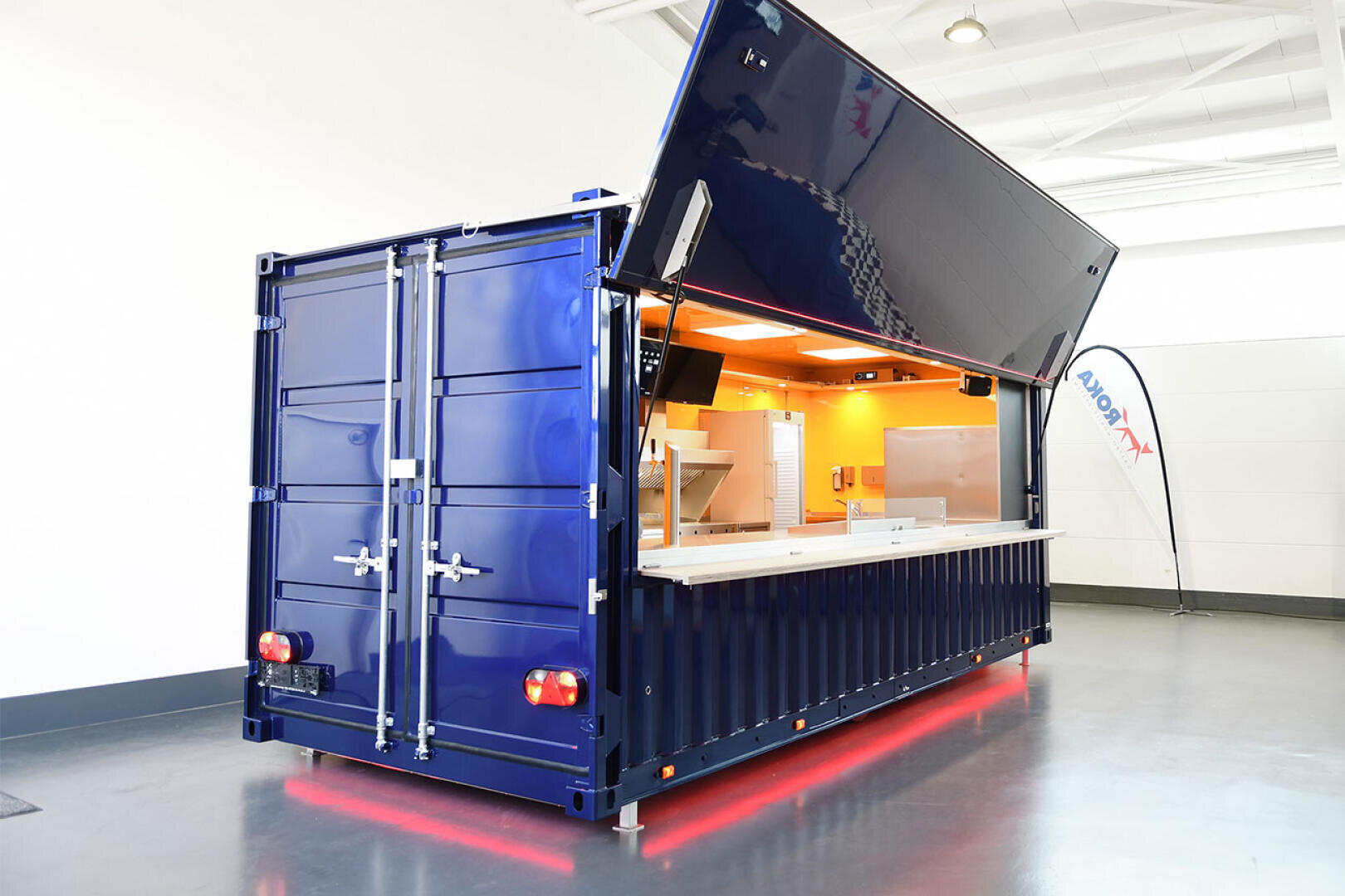 Ein blauer Schiffscontainer, der zu einem Imbissstand mit offenem Ausgabeschalter und Küchenausstattung im Inneren umgebaut wurde.