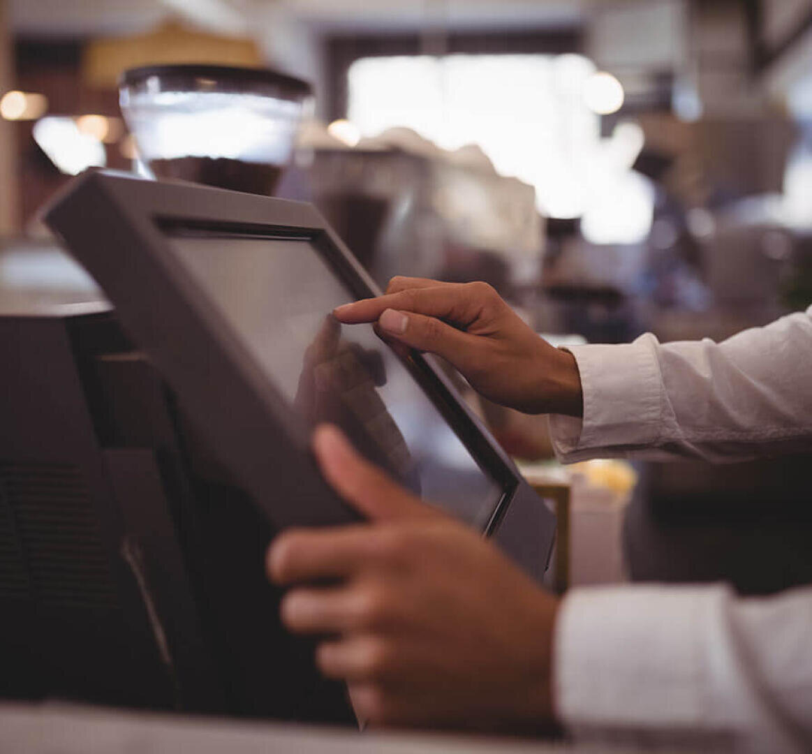 Die Hand einer Person, die an einer Theke ein Touchscreen-Kassenterminal bedient.