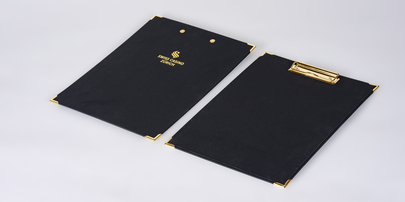 Zwei schwarze Schreibunterlagen mit goldenen Akzenten an den Ecken; auf einer ist das Logo des Swiss Casino Zürich abgebildet.